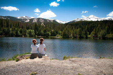 little girls sitting by a mountain lake