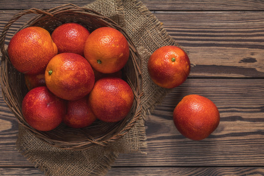 Blood orange fruit in a wicker basket on dark wooden table.