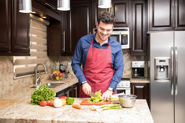 Young man preparing salad in kitchen