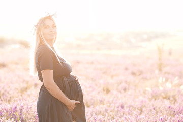 Fototapeta na wymiar Happy pregnant woman standing in lavender field. Looking at camera. Selective focus.