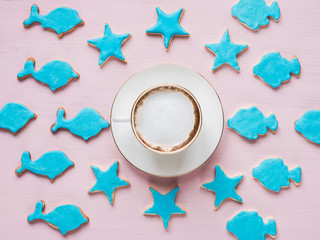Cup with fragrant coffee and a fresh, festive cookies in blue glaze of different shapes on a pink background. Top view of a close-up. Holiday, romance, beauty