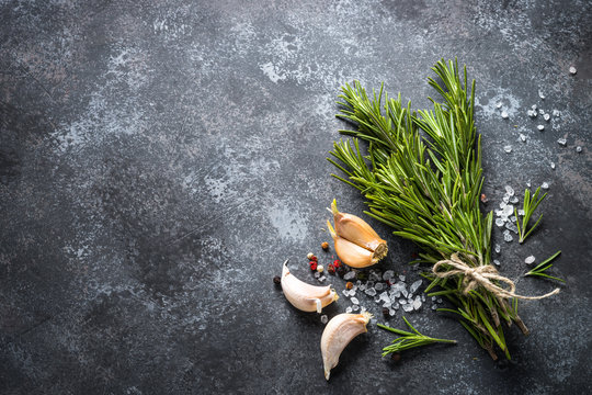 Sprigs of rosemary, pepper and garlic on a dark stone background
