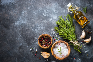 Sprigs of rosemary, pepper and garlic on a dark stone background