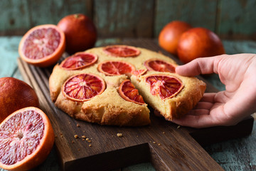 Homemade cake. Woman hand holding piece of fruit cake with blood oranges on oak board