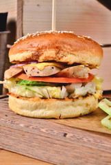 Top view Fresh homemade burger with chicken, salad, cheese, onion, cucumber, tomato, sause and dark beer on a wooden board, table background. Juicey gourmet roll bread, fast food concept. Text place
