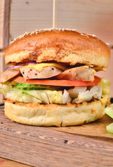 Top view Fresh homemade burger with chicken, salad, cheese, onion, cucumber, tomato, sause and dark beer on a wooden board, table background. Juicey gourmet roll bread, fast food concept. Text place