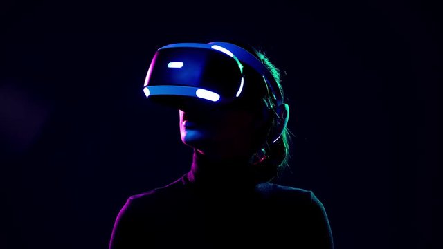 Young woman in VR headset looks around and wonders how amazing. Virtual reality helmet on black background