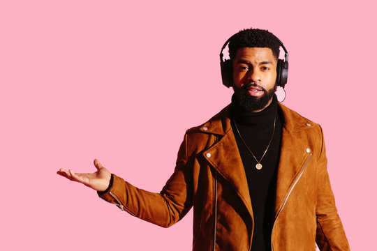 Portrait of a cool man with beard and headphones gesturing with his hand out isolated on pink studio background