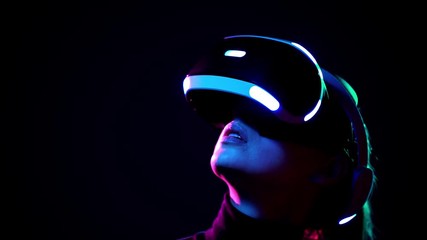 Young woman in VR headset looks around and wonders how amazing. Virtual reality helmet on black background - Powered by Adobe