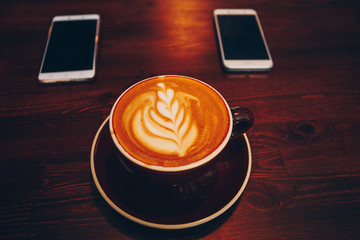 A cup of coffee on wooden surface with mobiles in cafe