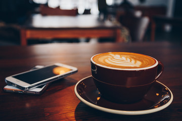 A cup of coffee on wooden surface with mobiles in cafe