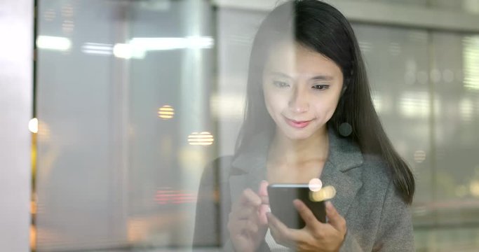 Business woman look at smart phone with window glass reflection at night