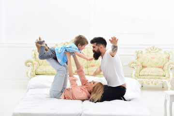 Obraz na płótnie Canvas Parents with happy faces pay attention to kid, play like plane. Mother and father play with cute son. Happy family concept. Young family spend time together on bed, luxury interior background.