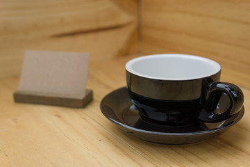 selective focus, close up of empty black coffee cup on the corner of wooden room or box with brown stand label. food or interior concept.