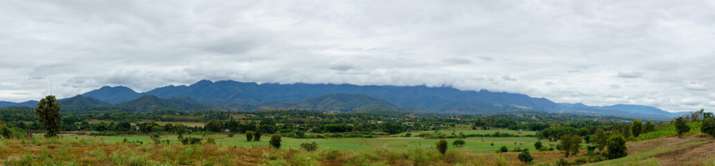 Fototapeta na wymiar panorama landscape of field and local village with sky and cloud and layer of mountain background