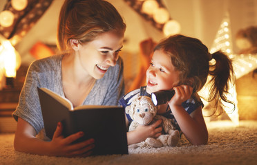 mother and child daughter reading a book and a flashlight before going to bed