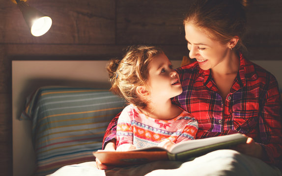 mother and child reading book in bed before going to sleep .