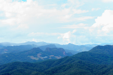 Fototapeta premium Amazing wild nature view of layer of mountain forest landscape with cloudy sky at winter season. Natural green scenery of cloud and mountain slopes background.
