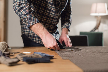 Fototapeta premium Closeup cutting brown plaid wool fabric. the line pattern. Young man working as a tailor and using a sewing machine in workshop.