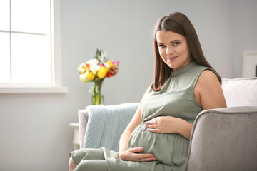 Obraz na płótnie Canvas Beautiful pregnant woman sitting in armchair at home