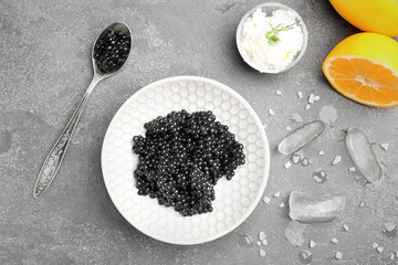 Spoon and bowl with delicious black caviar on grey background