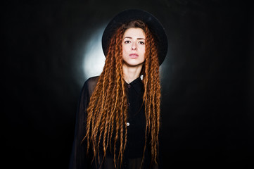 Studio shoot of girl in black with dreads and hat at black background.