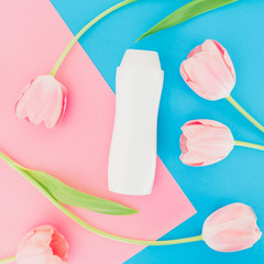 Shampoo bottle and tulips flowers on pink and blue background. Flat lay, top view