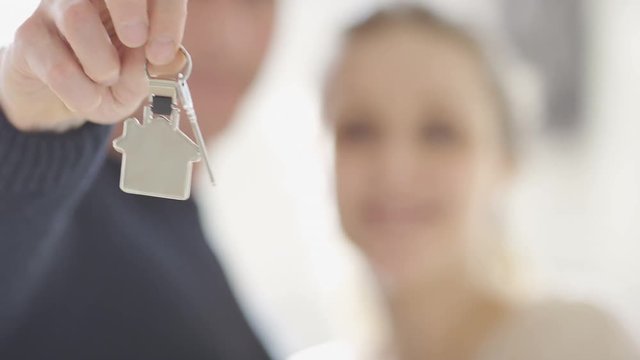 Blurred couple holding property keys to camera in the foreground, in slow motion
