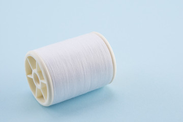 spool of  white sewing thread on blue background with copy space