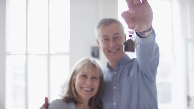 Mature older couple holding keys to a property to camera