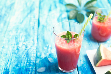 Fresh watermelon smoothie in two glasses with a straw and a piece of fruit on a blue wooden rustic background wth copyspace