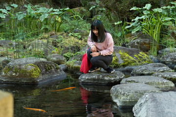 Young asian girl posing in a japanese garden near a pond of fish