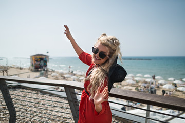 Young attractive woman in bright red dress dances on the city promenade. Elegant blonde girl active...