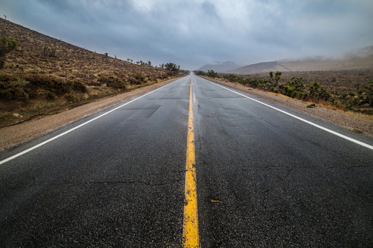 Empty wet desert asphalt pavement road with yellow highway marking lines.