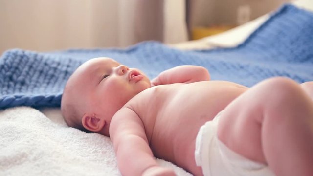 A little cute little boy lies on a bed in a diaper, his tongue out. HD, 1920x1080. slow motion.