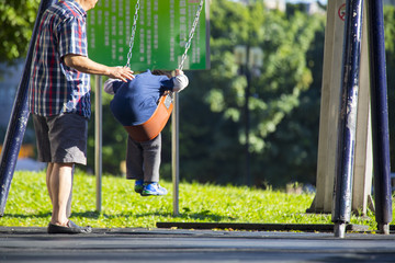 Taipei, Taiwan, the sun shines in the autumn park. The grandfather swings with his grandson.