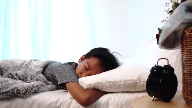 Young Asian boy sleeping on a white bed and awake to turn off alarm clock.
