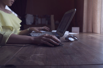 Close up of a woman hands working with a laptop and a mouse in a home interior or on desk wood beside window and light shade