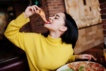 Lustiges Brunettemädchen im gelben Pullover, der Pizza im Restaurant isst.