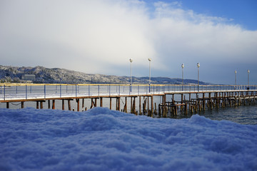 Seascape with old destroyed pier on the background of snow-capped hills.