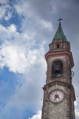 ancient bell tower close-up with clock and clouds in the background