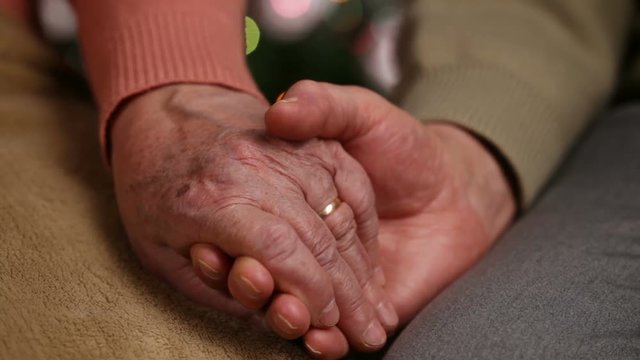Senior hands of woman and man holding in front of christmas lights - old age concept, together forever, extreme closeup