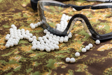 balls airsoft bbs and protective glasses on a camouflage background