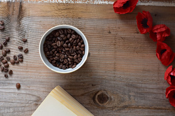 Coffee beans, old book and red flowers on wooden background