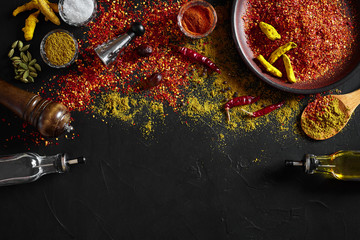 Fototapeta na wymiar Cooking using fresh ground spices with big and small bowls of spice on a black table with powder spillage on its surface, overhead view with copyspace