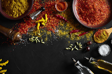 Cooking using fresh ground spices with big and small bowls of spice on a black table with powder spillage on its surface, overhead view with copyspace