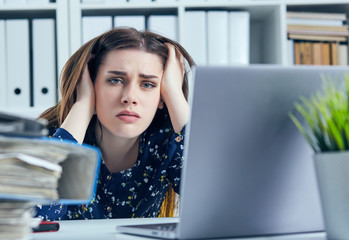 Tired and exhausted woman looks at the mountain of documents propping up her head with her hands.