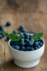 Fresh blueberries heap in white bowl in side view with copy space on wood table for background in vintage tones. Blueberry is healthy and delicious fruits which have high antioxidant and vitamin C.