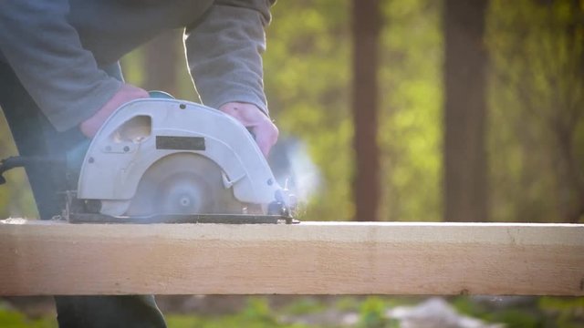 Sawing wooden beam lengthways with a circular hand saw outdoors in summer