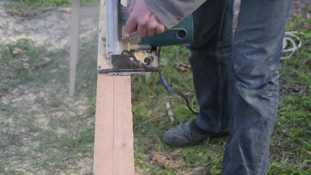 Sawing wooden beam lengthwise with a circular hand saw outdoors in summer